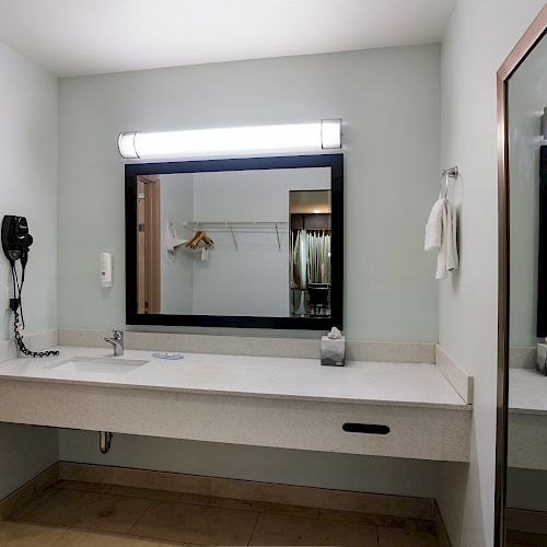 A bathroom vanity area with a wall-mounted mirror, countertop with sink, a towel, and a hairdryer. An adjacent door opens to a closet space.
