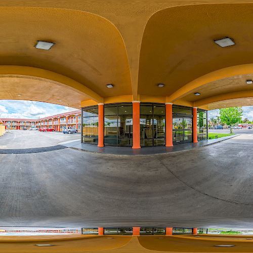 This image shows a 360-degree view of a concrete driveway under a yellow portico with overhead lighting, next to a glass entrance door.